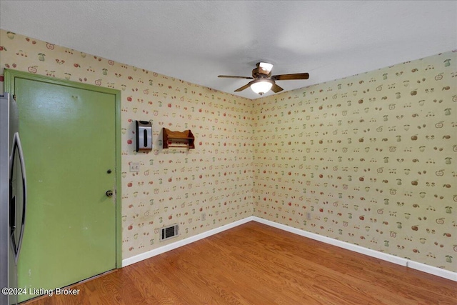 spare room with visible vents, ceiling fan, wood finished floors, baseboards, and wallpapered walls