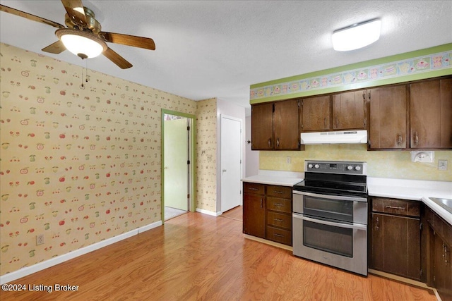 kitchen with under cabinet range hood, light countertops, double oven range, light wood finished floors, and wallpapered walls