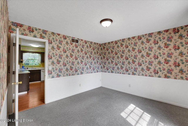 unfurnished room featuring a sink, visible vents, wainscoting, dark colored carpet, and wallpapered walls