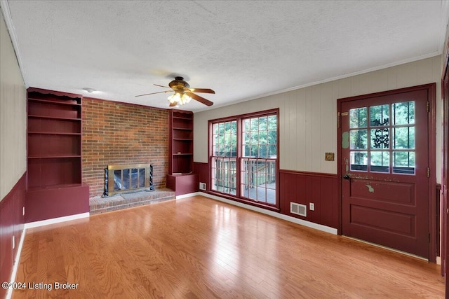 unfurnished living room with a textured ceiling, wood finished floors, visible vents, built in features, and a brick fireplace