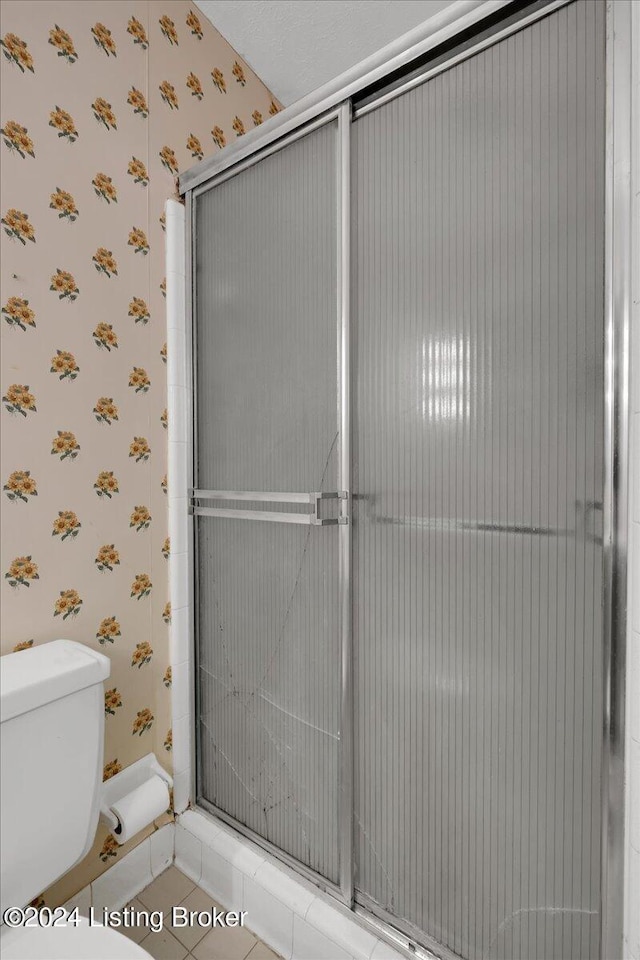 full bath featuring toilet, wallpapered walls, a shower stall, and tile patterned floors