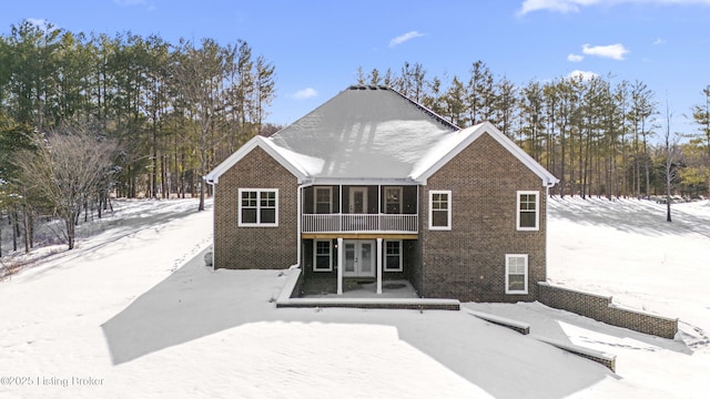 snow covered back of property with brick siding, a sunroom, and french doors