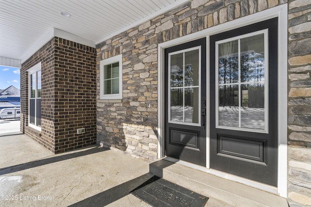 doorway to property with stone siding, a porch, and brick siding