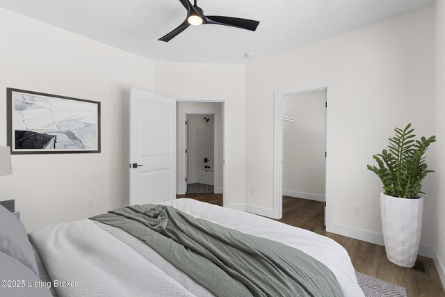 bedroom with ceiling fan, a spacious closet, wood finished floors, and baseboards