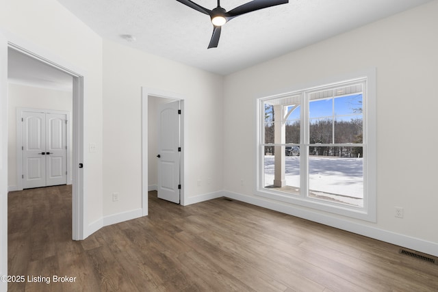 empty room featuring a ceiling fan, visible vents, baseboards, and wood finished floors