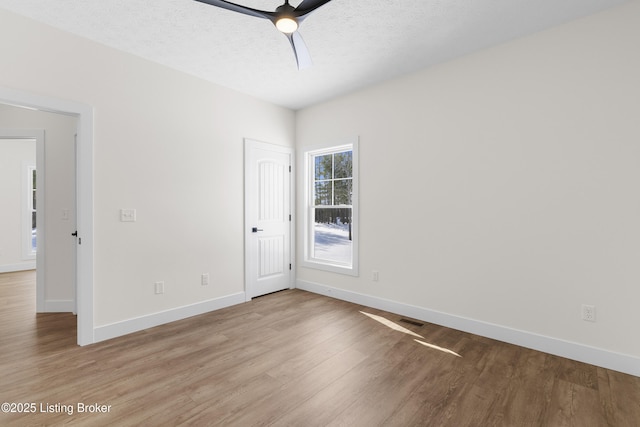 unfurnished room featuring visible vents, baseboards, a ceiling fan, wood finished floors, and a textured ceiling