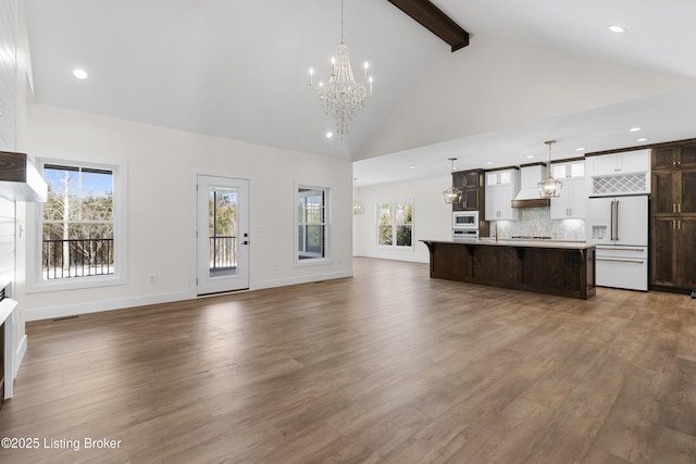 unfurnished living room with a notable chandelier, wood finished floors, high vaulted ceiling, beamed ceiling, and baseboards