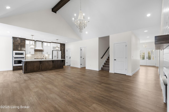 unfurnished living room with dark wood finished floors, high vaulted ceiling, stairway, a chandelier, and beamed ceiling