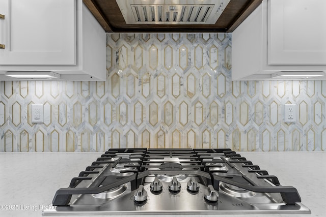 details featuring white cabinets, stainless steel gas cooktop, extractor fan, and decorative backsplash