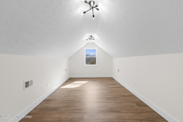 bonus room featuring visible vents, vaulted ceiling, a textured ceiling, wood finished floors, and baseboards