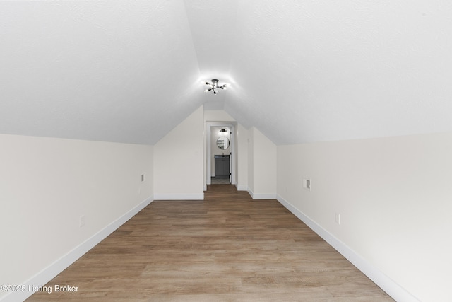 additional living space with vaulted ceiling, light wood-style flooring, baseboards, and a textured ceiling