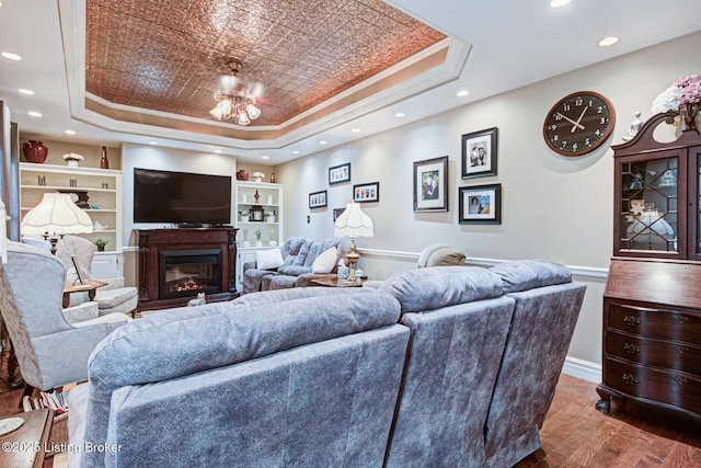 living area with built in features, a tray ceiling, crown molding, and wood finished floors