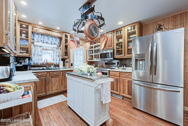 kitchen featuring light wood-style flooring, glass insert cabinets, stainless steel appliances, and a sink