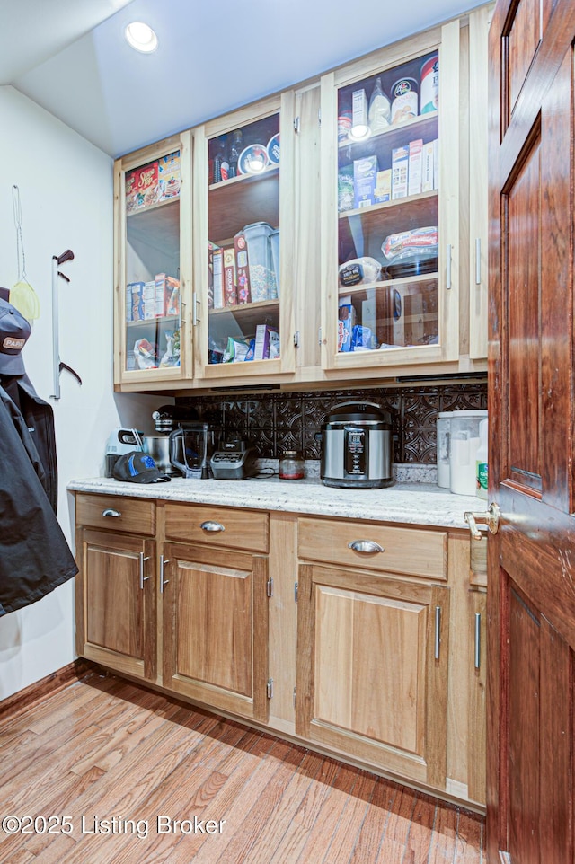 kitchen featuring light stone countertops, light wood-style floors, and glass insert cabinets