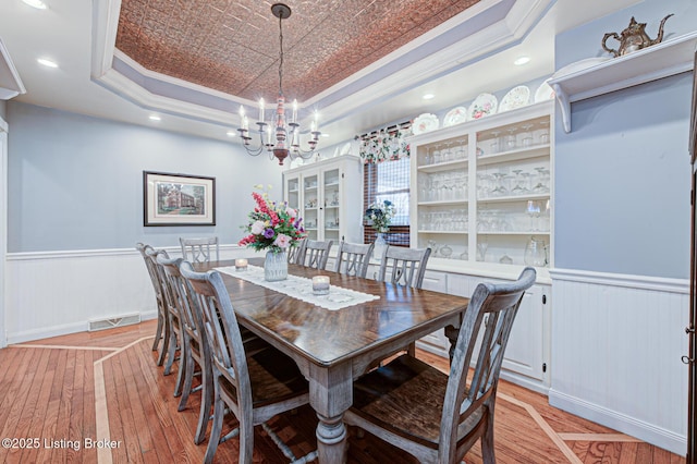 dining area with a wainscoted wall, visible vents, a raised ceiling, and crown molding