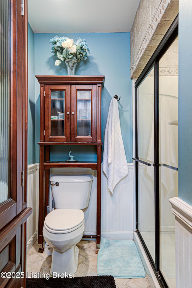 bathroom featuring wainscoting, a shower with shower door, and toilet