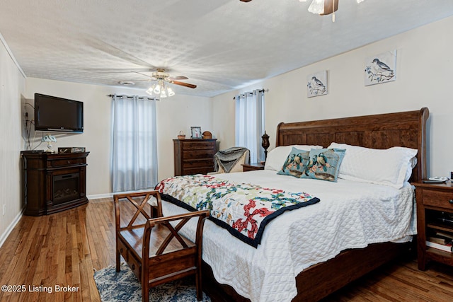 bedroom featuring ceiling fan, a textured ceiling, baseboards, and wood finished floors