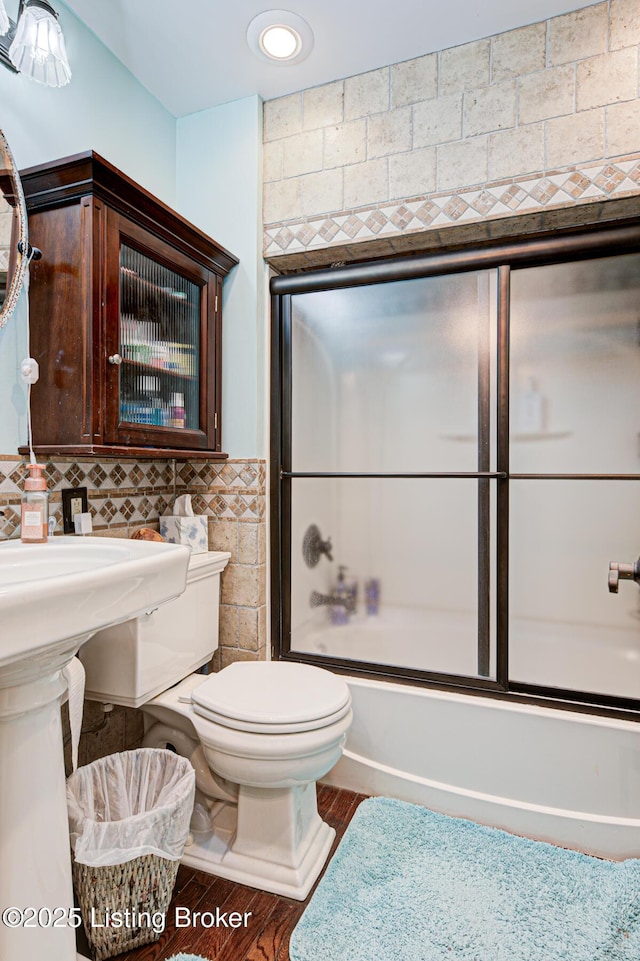 full bathroom with enclosed tub / shower combo, tile walls, toilet, and wood finished floors