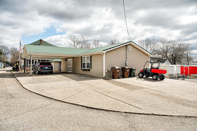 view of side of property with an attached carport, metal roof, and driveway