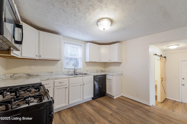 kitchen featuring black appliances, a sink, wood finished floors, white cabinetry, and a barn door