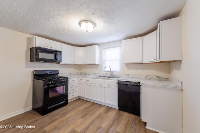 kitchen with baseboards, light wood-style floors, white cabinets, black appliances, and a sink