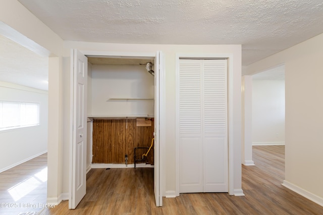 hall with a textured ceiling, baseboards, and wood finished floors