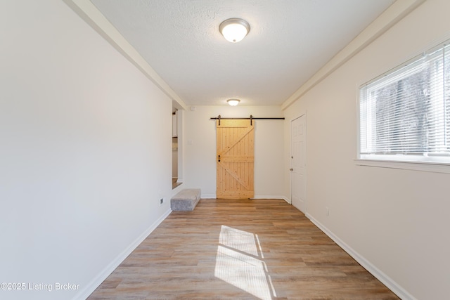 hallway featuring a barn door, baseboards, a textured ceiling, and light wood finished floors