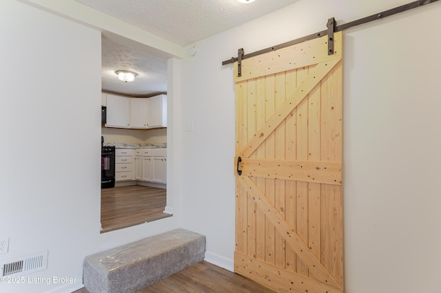 interior space with a barn door, wood finished floors, visible vents, and a textured ceiling