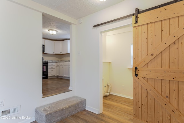 corridor featuring visible vents, a textured ceiling, wood finished floors, a barn door, and baseboards