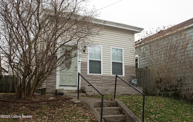 view of side of home with stone siding, fence, and entry steps