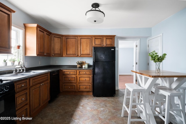 kitchen featuring dark countertops, black appliances, brown cabinetry, and a sink