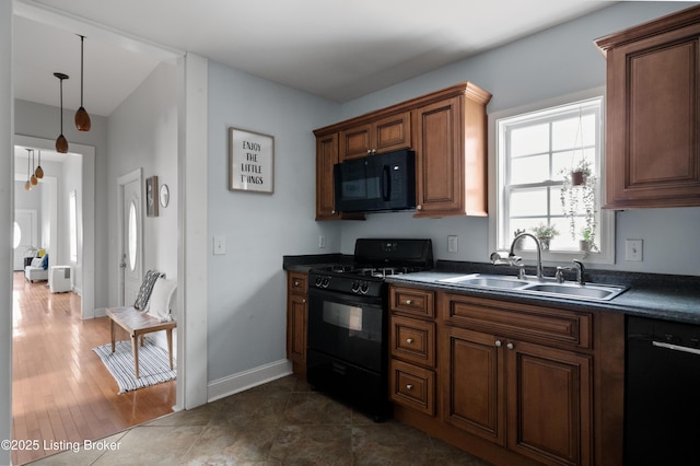 kitchen featuring black appliances, a sink, dark countertops, brown cabinetry, and baseboards