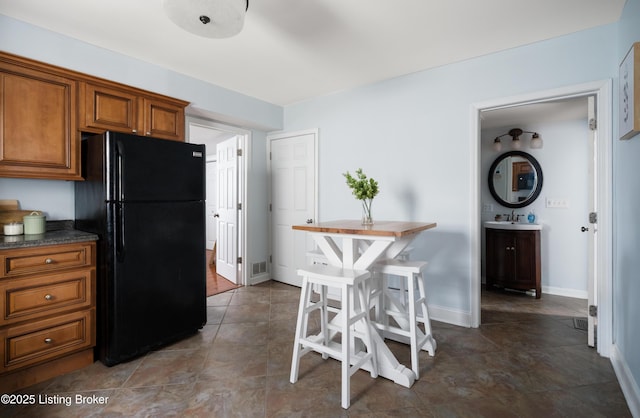 kitchen with visible vents, freestanding refrigerator, a sink, dark countertops, and brown cabinets