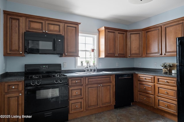 kitchen with brown cabinets, dark tile patterned flooring, black appliances, a sink, and dark countertops