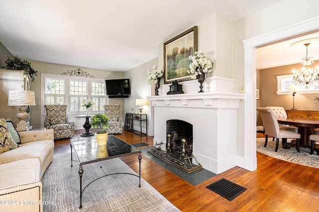 living room with an inviting chandelier, wood-type flooring, a brick fireplace, and visible vents