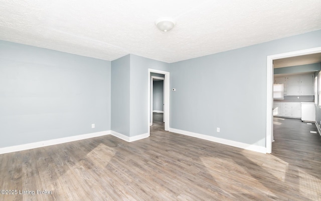 unfurnished room with a textured ceiling, baseboards, and wood finished floors