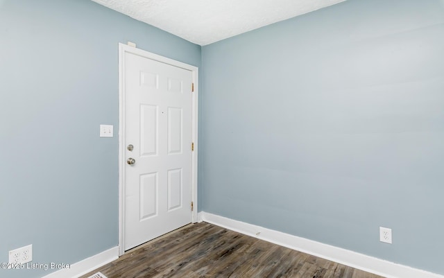 spare room with dark wood-style flooring, a textured ceiling, and baseboards