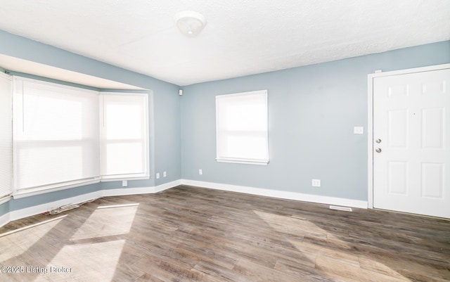 unfurnished room with a textured ceiling, baseboards, and wood finished floors