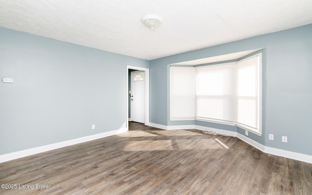 empty room featuring a textured ceiling, baseboards, and wood finished floors