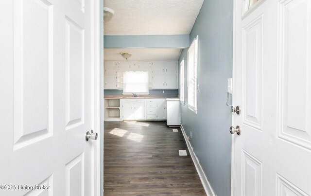 hall with a textured ceiling, baseboards, dark wood-type flooring, and a sink