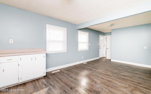 empty room featuring dark wood-style flooring, visible vents, a textured ceiling, and baseboards