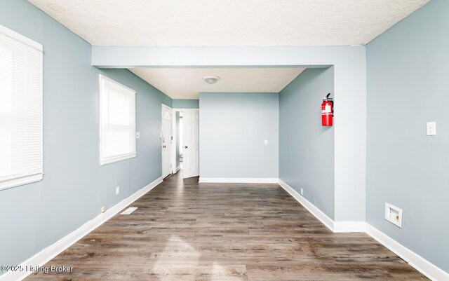 unfurnished room with a textured ceiling, baseboards, and wood finished floors