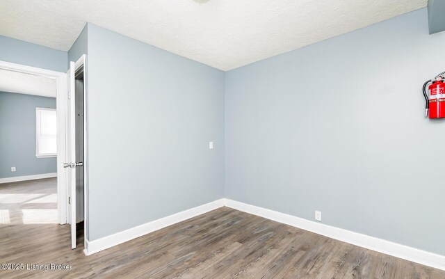 spare room with a textured ceiling, wood finished floors, and baseboards