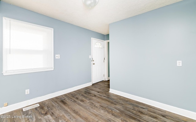 empty room featuring a textured ceiling, wood finished floors, visible vents, and baseboards