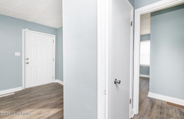 hall with wood finished floors, visible vents, and baseboards