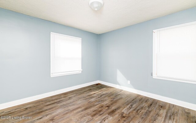 spare room with a textured ceiling, baseboards, and wood finished floors