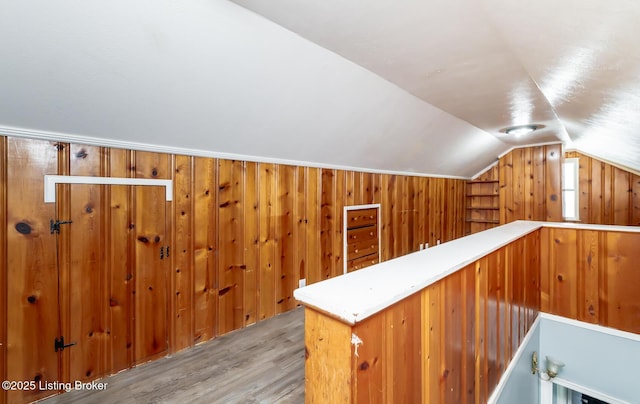 bonus room featuring light wood-type flooring, vaulted ceiling, and wood walls