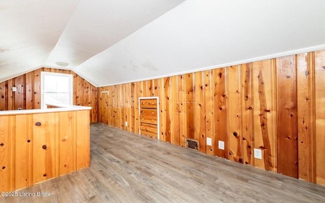 bonus room with lofted ceiling, wood walls, wood finished floors, and visible vents