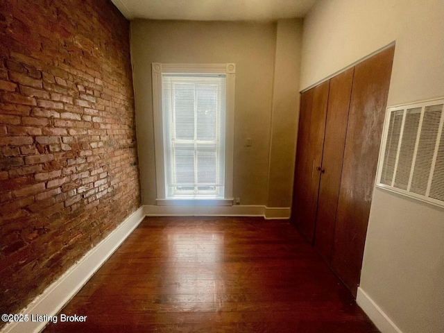 corridor with brick wall, dark wood finished floors, and baseboards