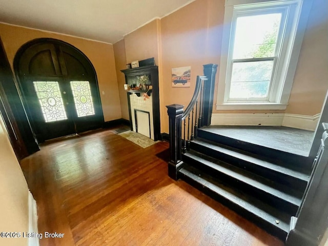 entryway featuring arched walkways, french doors, stairway, a fireplace with flush hearth, and wood finished floors